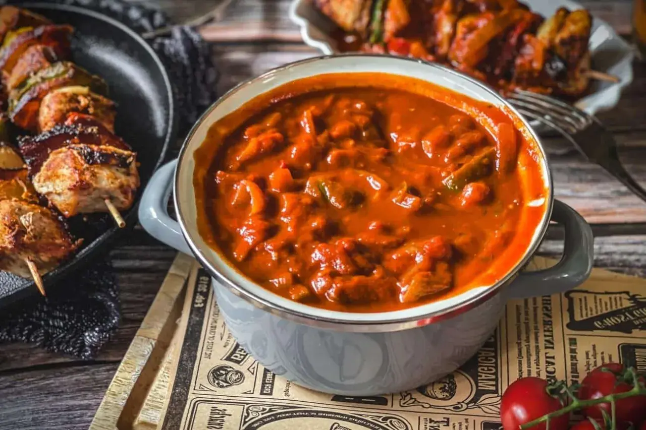 Herzhafte schaschlik sauce wie im imbiss, mit Fleischstücken und Paprika, dane daneben gegrillte Spieße.