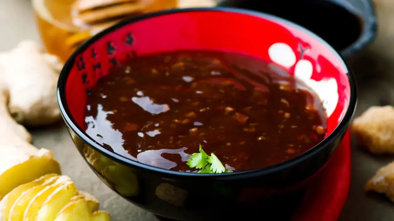 Eine Schüssel mit glänzender Teriyaki-Sauce, umgeben von Ingwer und braunem Zucker. Was ist Teriyaki? Eine süß-salzige Glasur für Fleisch und Fisch.
