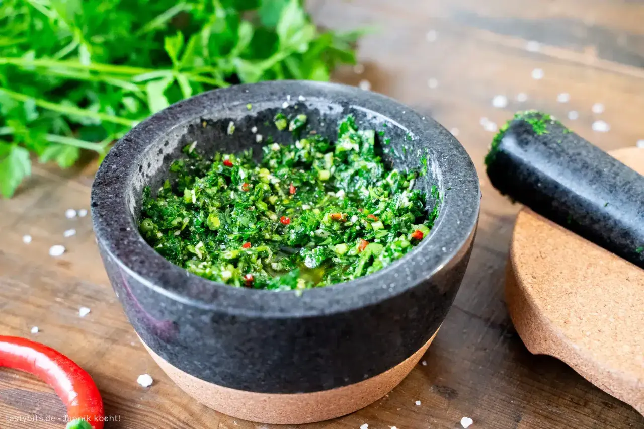 Frisches Chimichurri-Rezept im Mörser, bereit zum Verfeinern von Grillgut. Kräuter, Chili und Öl duften verführerisch.