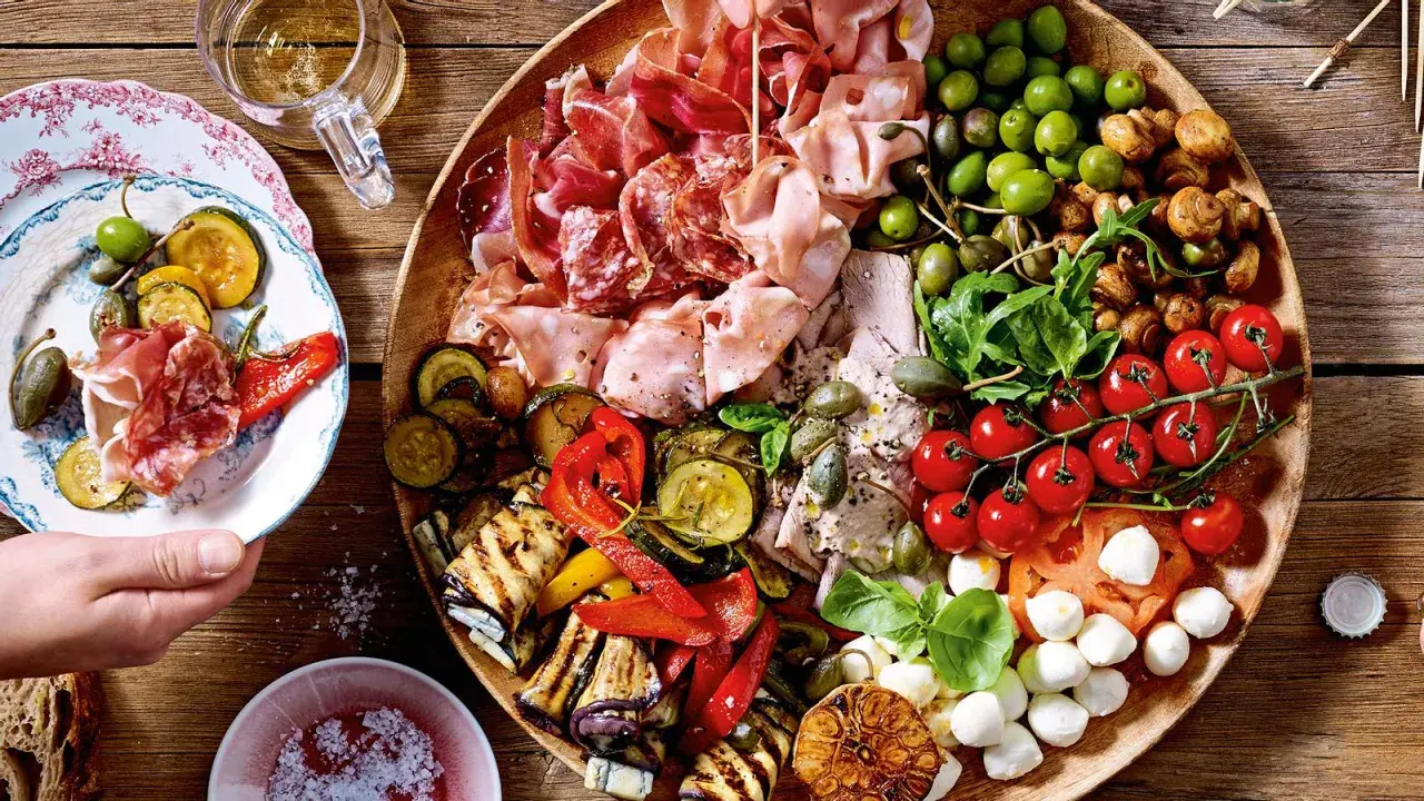 Vielfältige Antipasti Platte Ideen: Wurst, Käse, Oliven, gegrilltes Gemüse und frische Tomaten auf rustikalem Holzbrett.