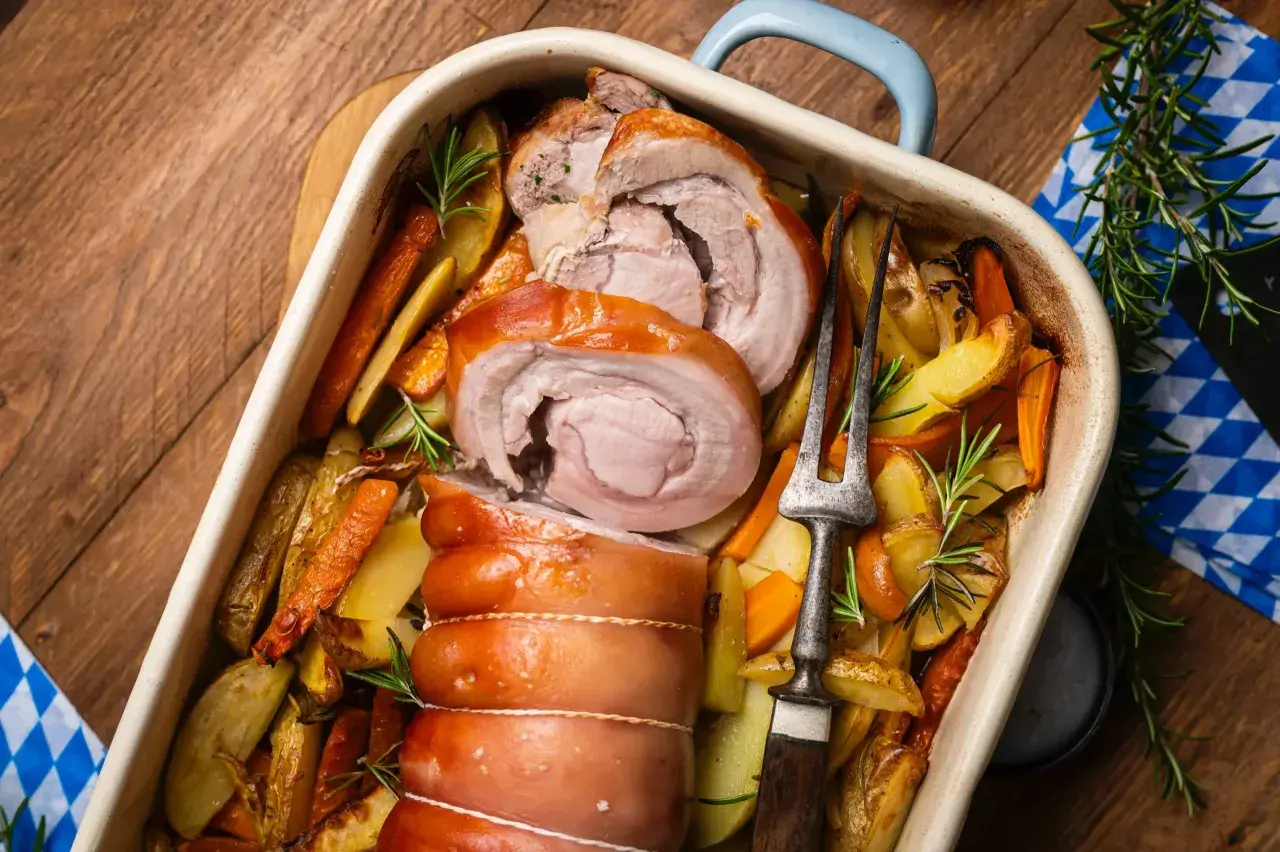 Saftiger **Rollbraten im Backofen** mit Rosmarinkartoffeln und Karotten, bereit zum Servieren.