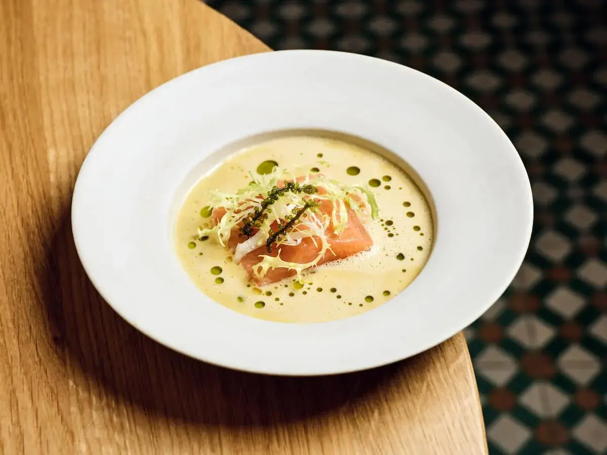 Ein Teller mit Lachs auf cremigem beurre blanc, garniert mit Salat und Kaviar.
