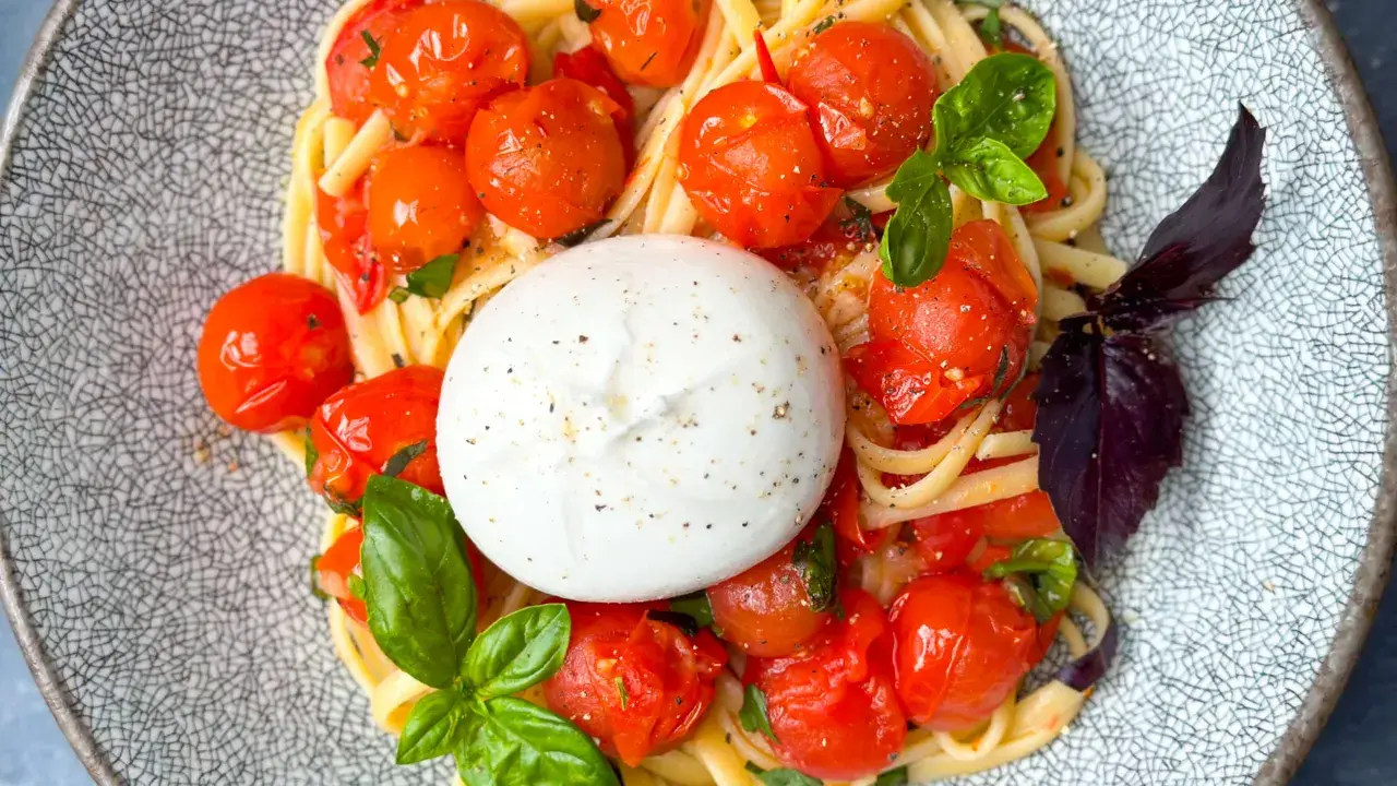 Ein cremiger Burrata Salat mit Pasta, Kirschtomaten und Basilikum auf einem gemusterten Teller.