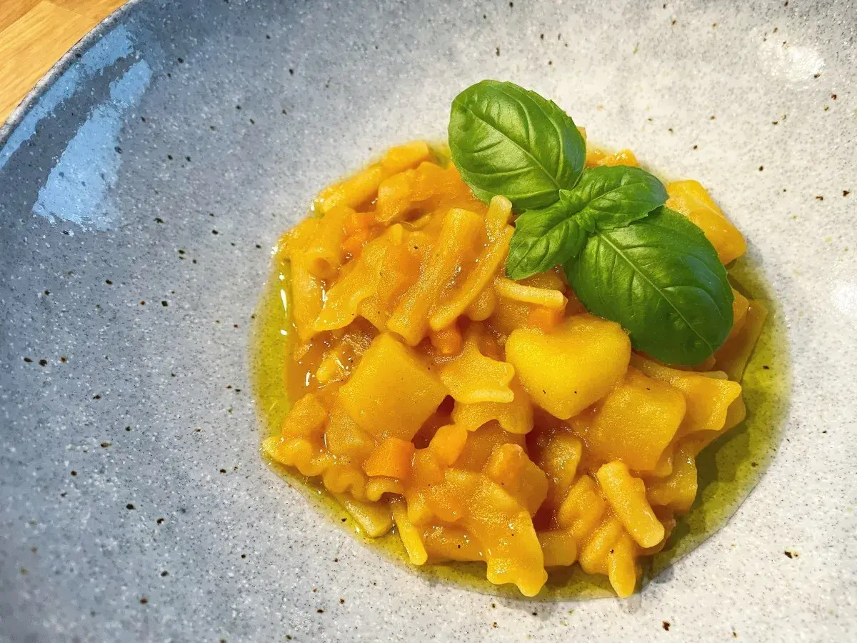 Herzhaftes Pasta e Patate mit Kartoffelstücken, Nudeln und frischem Basilikum in Olivenöl, serviert in einer grauen Schale.