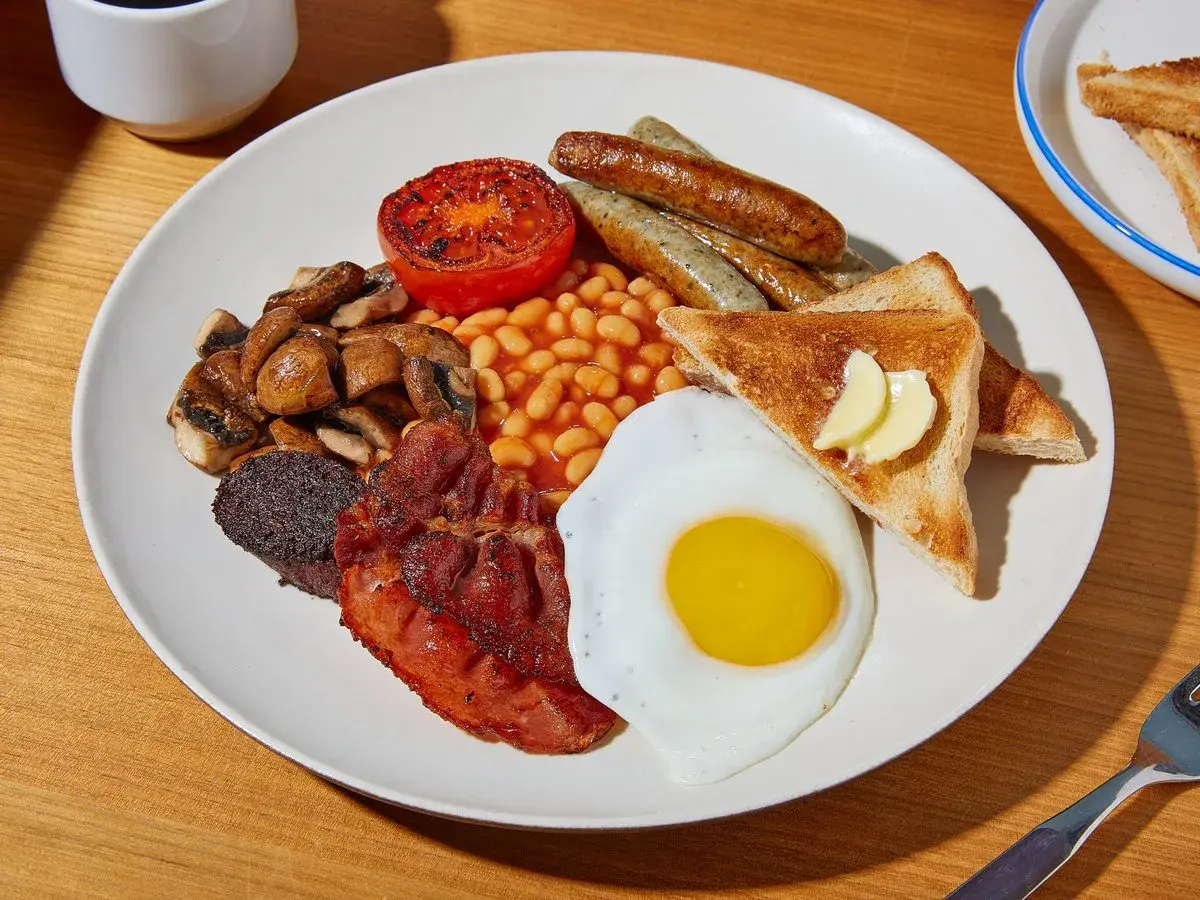 Ein üppiges **full English breakfast** mit Spiegelei, Speck, Würstchen, Bohnen, Pilzen, Tomate, Blutwurst und Toast.