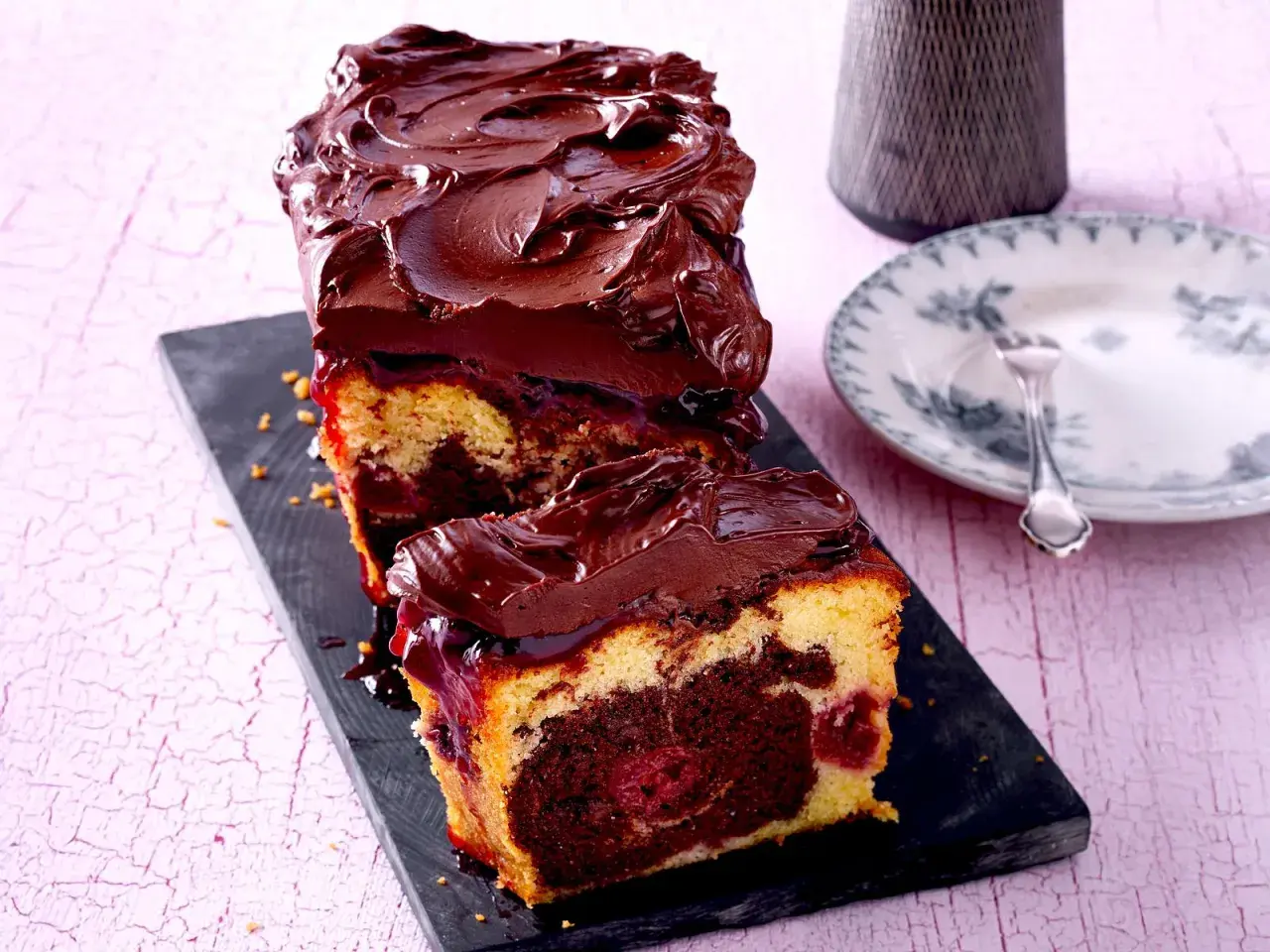 Saftiger Marmorkuchen mit Kirschen und dunkler Schokoladenglasur, auf einem schwarzen Brett serviert.