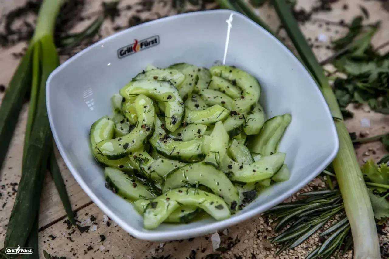 Frischer gurkensalat mit dill, garniert mit Pfeffer und Kräutern, serviert in einer weißen Schüssel.