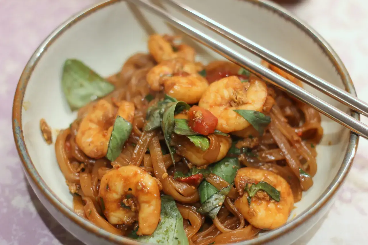 Pad Kee Mao mit Garnelen, Reisnudeln, Basilikum und Tomaten in einer Schüssel, bereit zum Genießen.