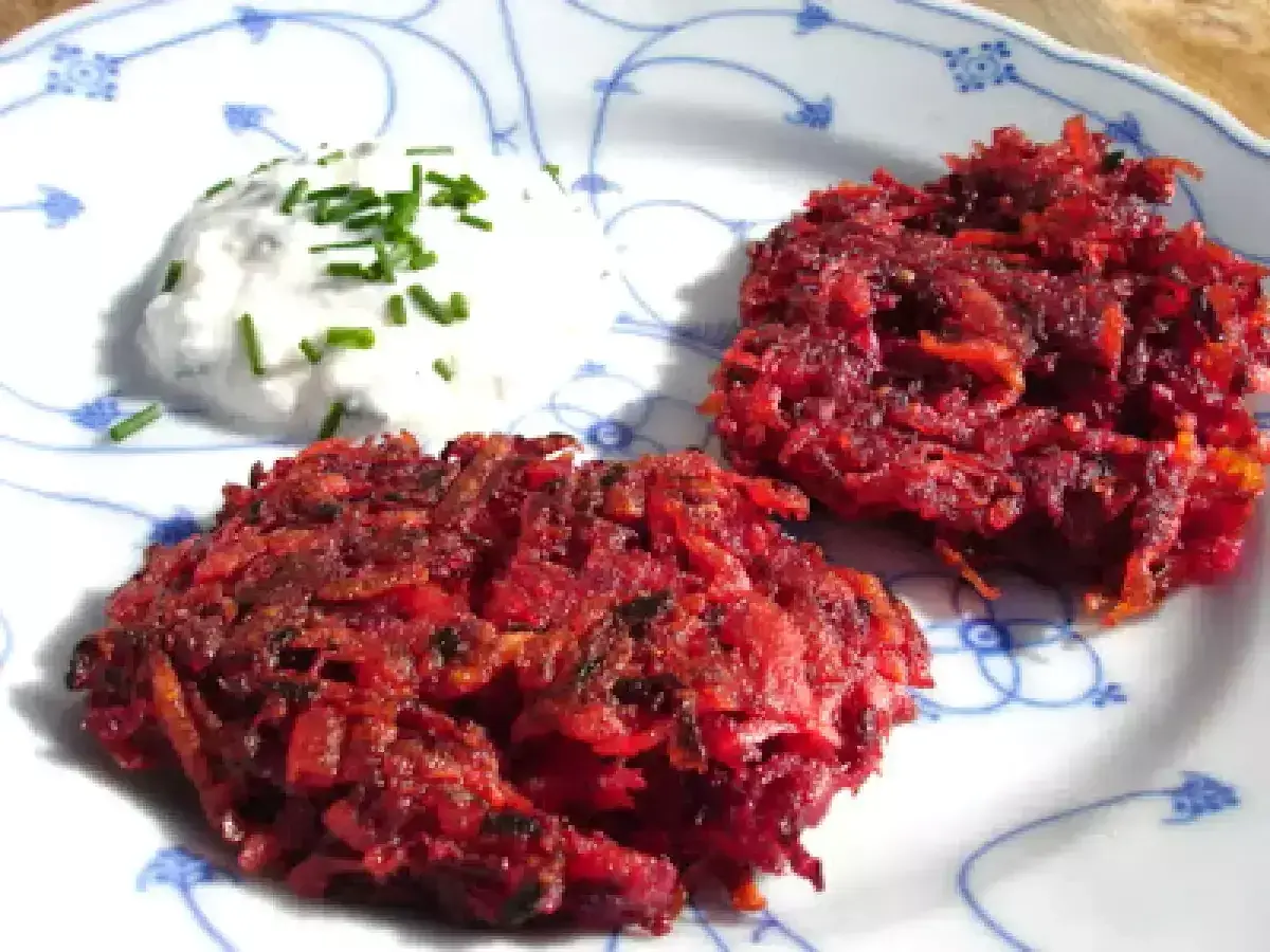 Zwei knusprige rote Bete Puffer paniert, serviert mit einem Klecks Kräuterquark auf einem Teller mit blauem Muster.
