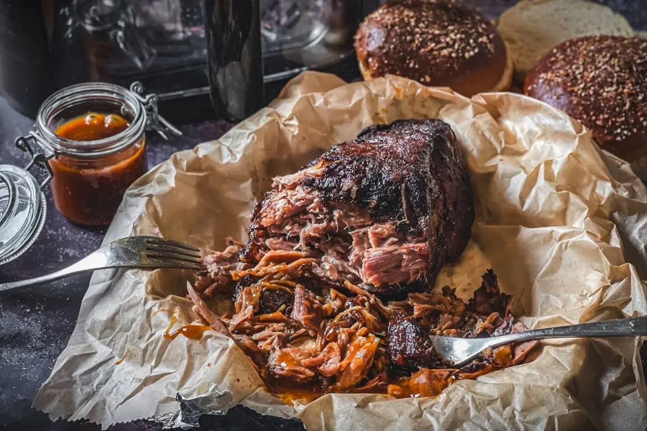 Pulled Pork aus dem Airfryer, saftig und zart, mit BBQ-Sauce beträufelt. Dazu passen die aufgeschnittenen Burgerbrötchen.