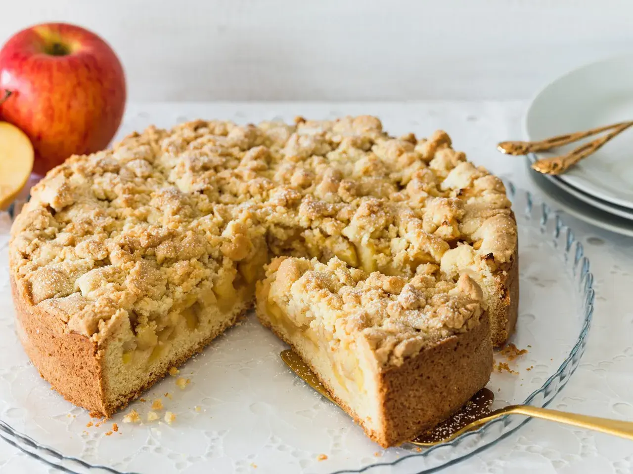 Ein saftiger, bester Apfelkuchen mit Streusel, bereit zum Servieren. Daneben liegen rote Äpfel.