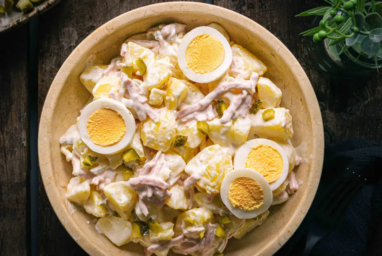 Schüssel mit Kartoffelsalat und Fleischsalat, garniert mit hartgekochten Eiern und Gewürzgurken.