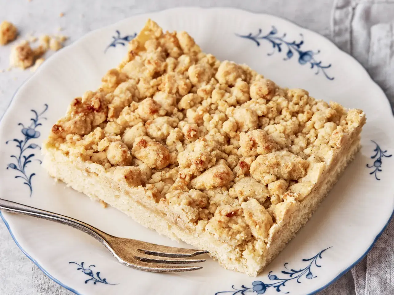 Ein Stück Streuselkuchen, wie von Oma nach DDR-Rezept, mit knusprigen Streuseln auf einem Teller mit blauem Rand.