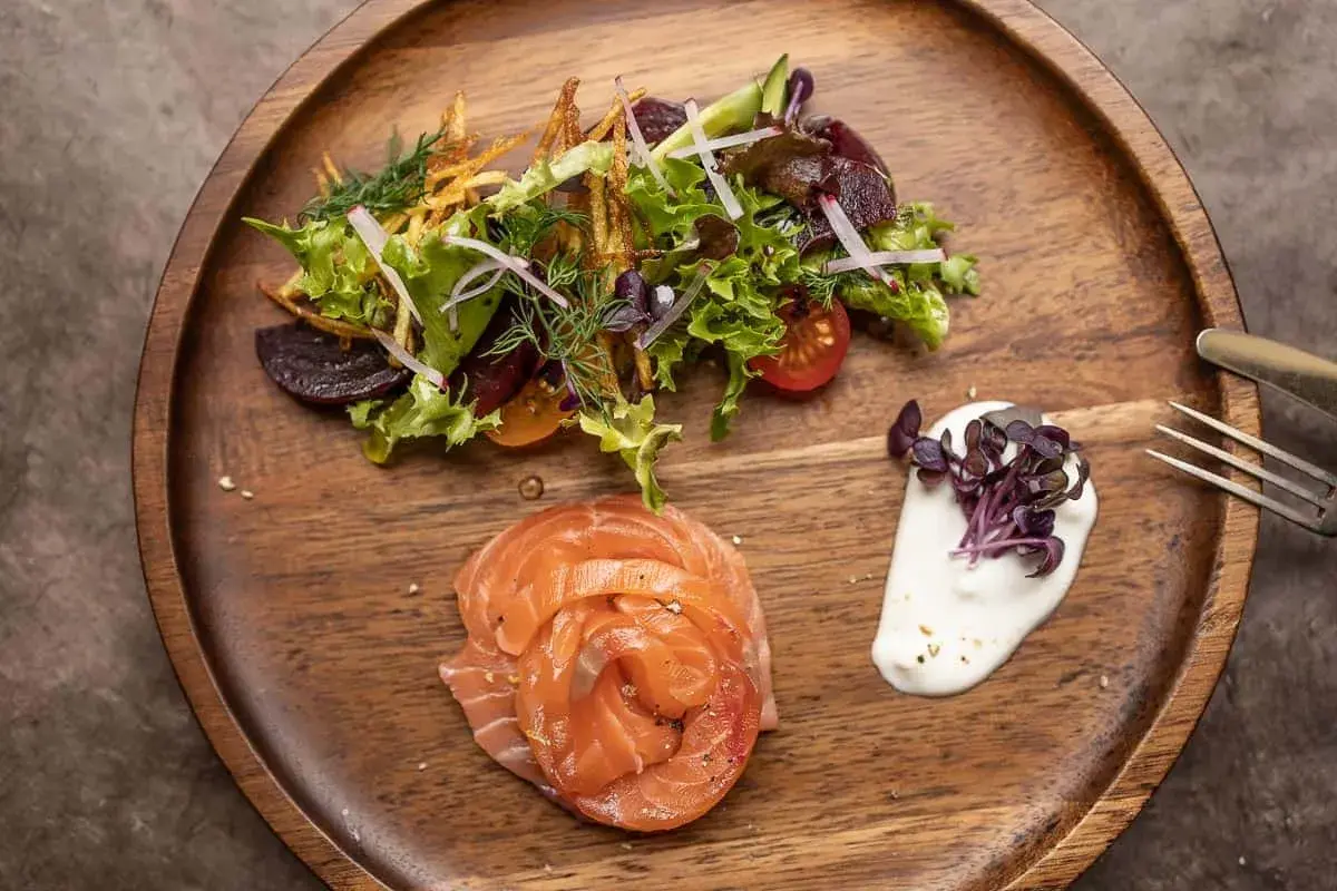 Gebeizter Lachs als Vorspeise, serviert mit einem frischen Salat und cremiger Sauce auf einem Holzbrett.