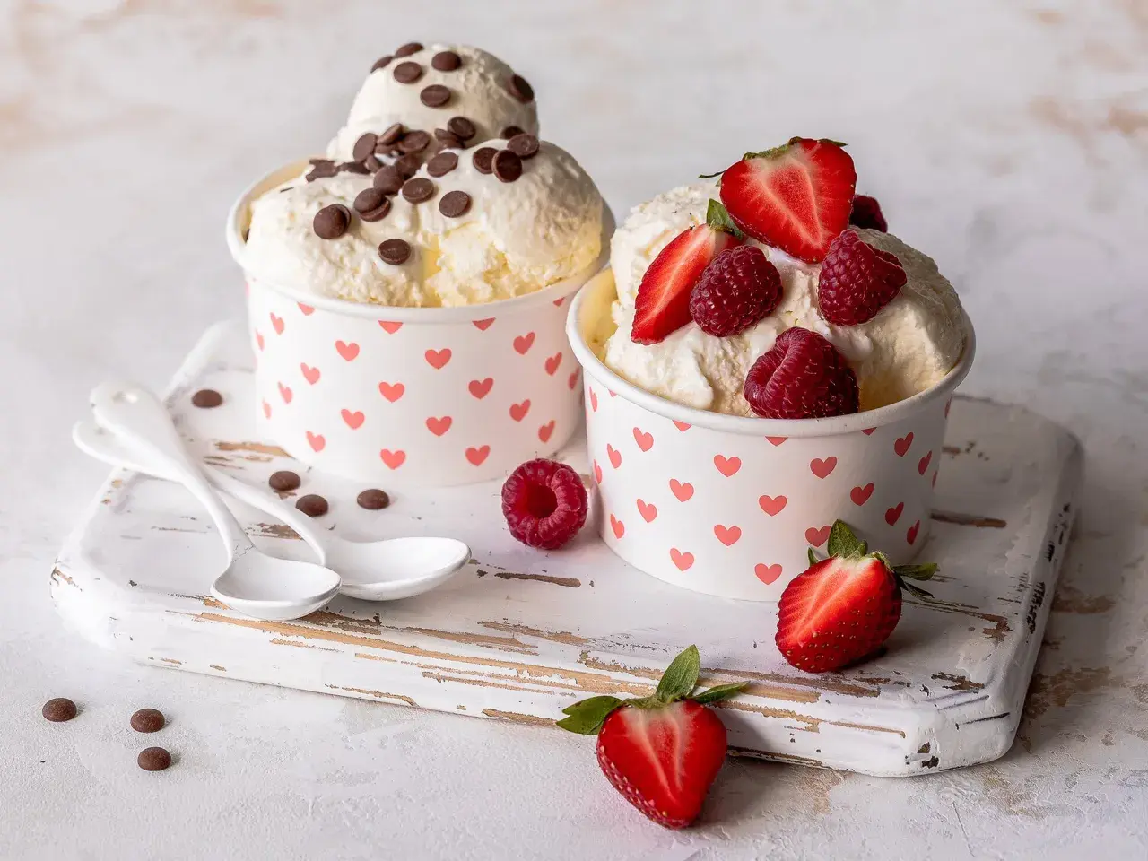 Zwei Becher mit cremigem Frozen Joghurt, einer mit Schokostückchen, der andere mit frischen Beeren. Ein leckeres Frozen Joghurt Rezept für heiße Tage.