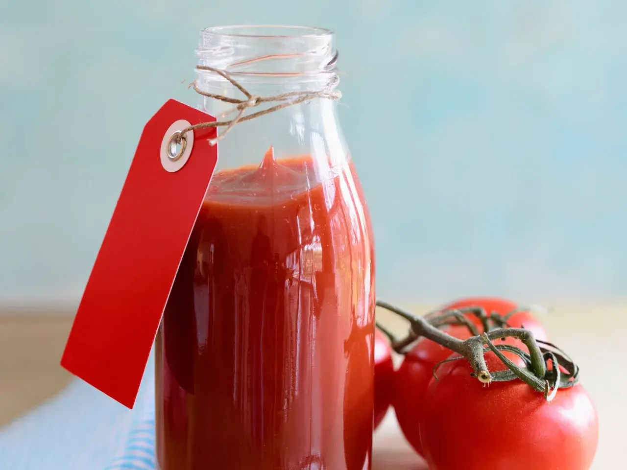 Glasflasche mit selbstgemachtem Tomatenketchup, rotem Anhänger und frischen Tomaten.