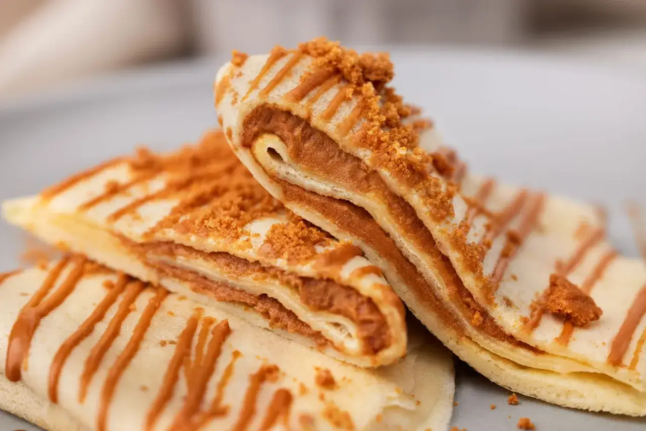 Gestapelte Pfannkuchen ohne Backpulver, gef&uuml;llt mit einer cremigen Karamellcreme und bestreut mit zerbr&ouml;selten Keksen.