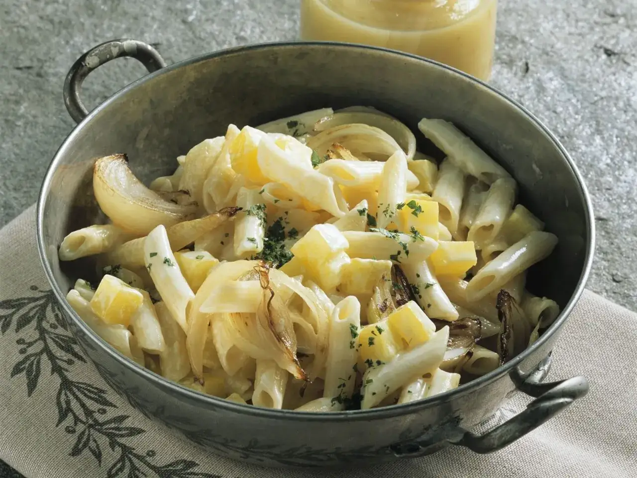 Herzhaftes Pasta e Patate mit Penne, Kartoffelwürfeln und karamellisierten Zwiebeln, garniert mit Petersilie.