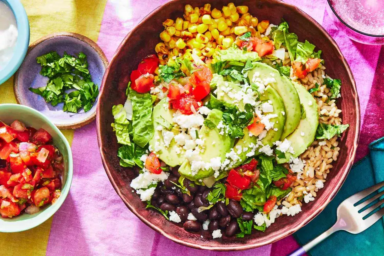 Ein köstliches Burrito Bowl Rezept mit Reis, schwarzen Bohnen, Mais, Avocado, Tomaten, Salat und Käse.
