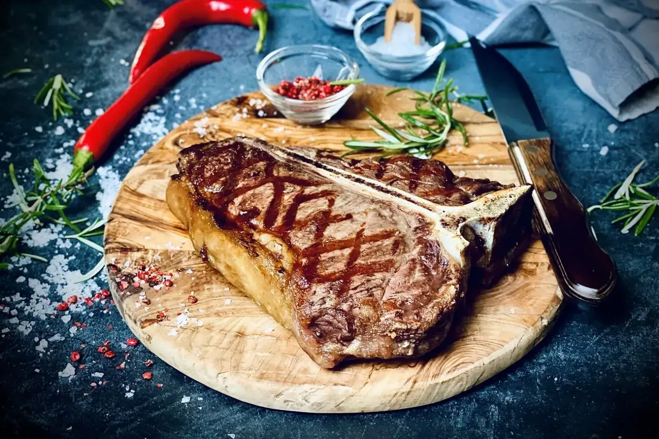 Perfekt gegrilltes T-Bone-Steak mit Grillstreifen, garniert mit Rosmarin, roten Chilis und grobem Salz. Ein Genuss f&uuml;r Fleischliebhaber!