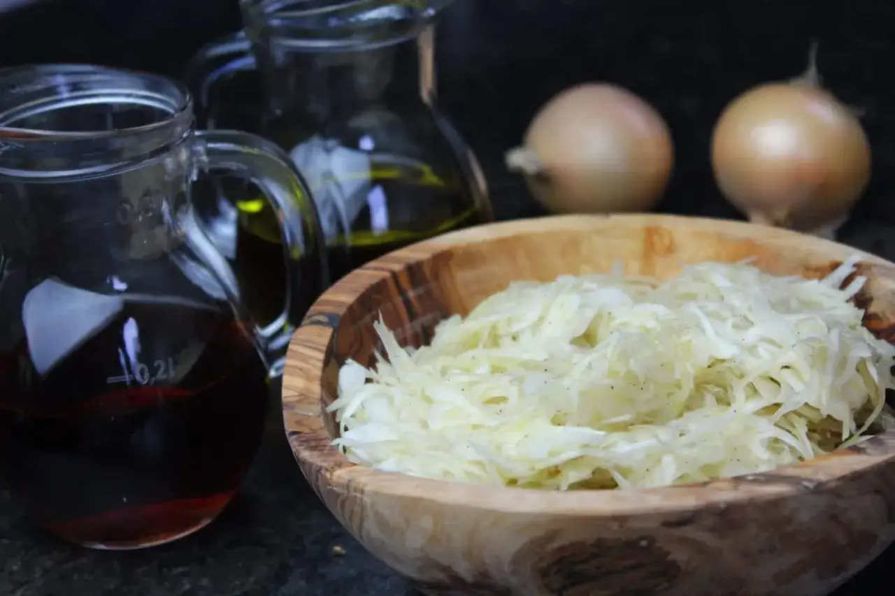 Frischer Krautsalat in Holzschale, daneben Olivenöl, Essig und Zwiebeln. Ein Hauch von Sahne könnte diesen griechischen Salat verfeinern.