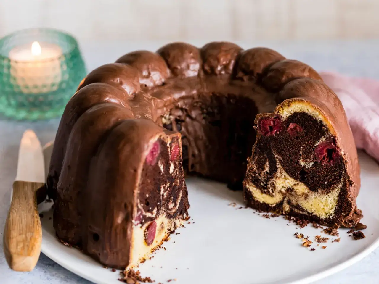 Ein saftiger Marmorkuchen mit Kirschen, &uuml;berzogen mit Schokoladenglasur, wartet auf dem Teller.