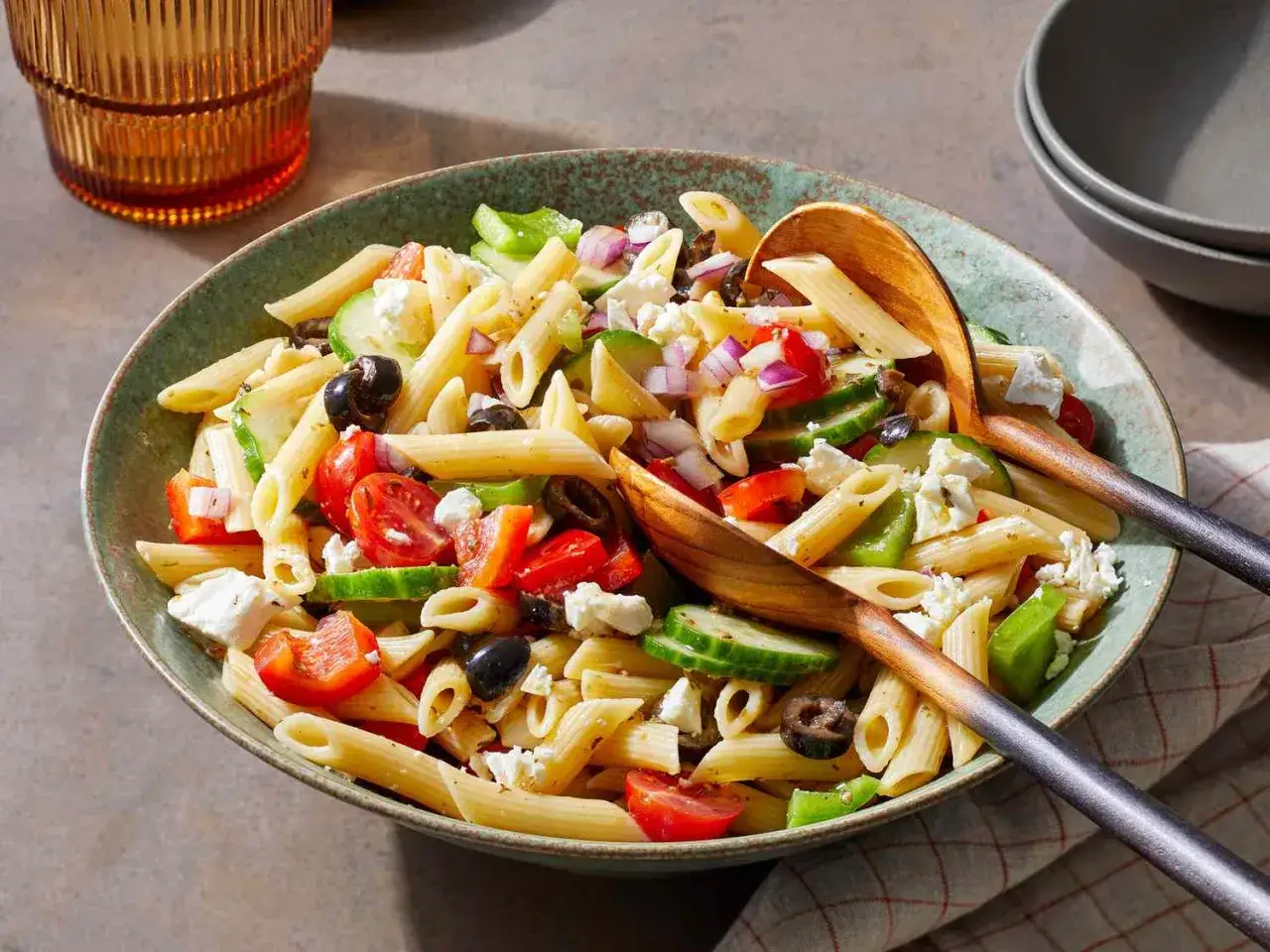 Ein bunter Kritharaki Salat mit Penne, Tomaten, Gurken, Oliven, Paprika und Feta. Serviert mit Holzsch&ouml;pfkellen.