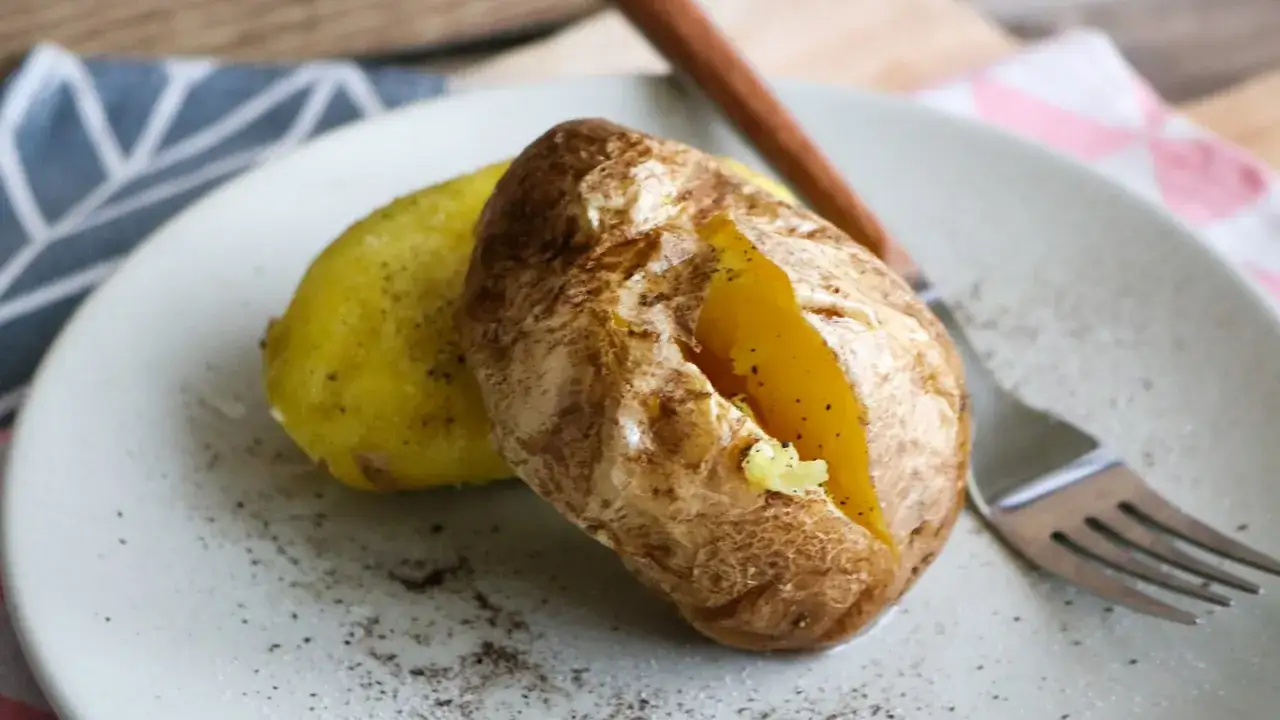 Zwei gebackene Kartoffeln, eine davon aufgeschnitten, mit Butter und Pfeffer, bereit zum Genuss. Perfekt, wenn es schnell gehen muss: Kartoffeln in der Mikrowelle.