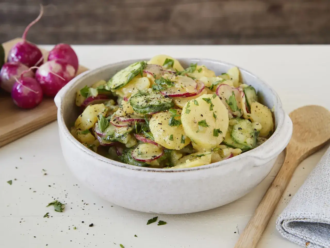 Herzhafter Kartoffelsalat mit Radieschen, Gurken und frischer Petersilie in einer Schüssel.