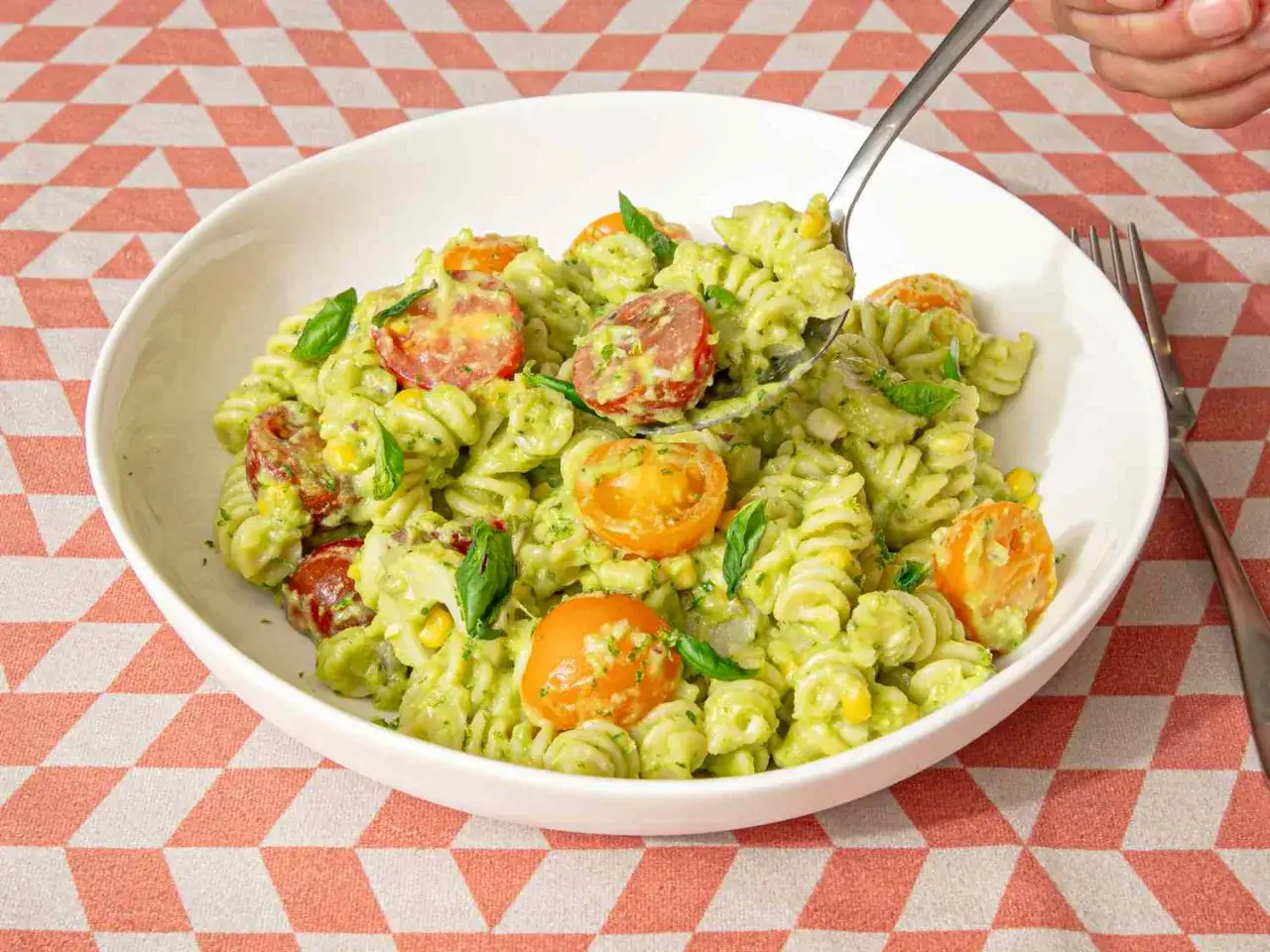 Fusilli-Pasta mit cremigem Avocado Basilikum Pesto, Kirschtomaten und Mais. Ein L&ouml;ffel wird gerade herausgenommen.
