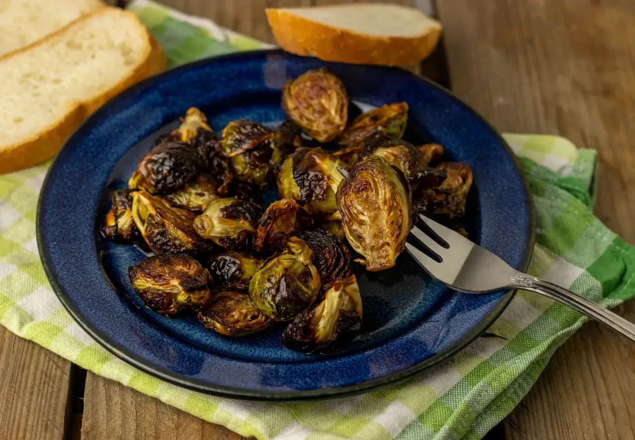 Knuspriger rosenkohl im backofen auf einem blauen Teller, daneben Brot und eine Gabel.