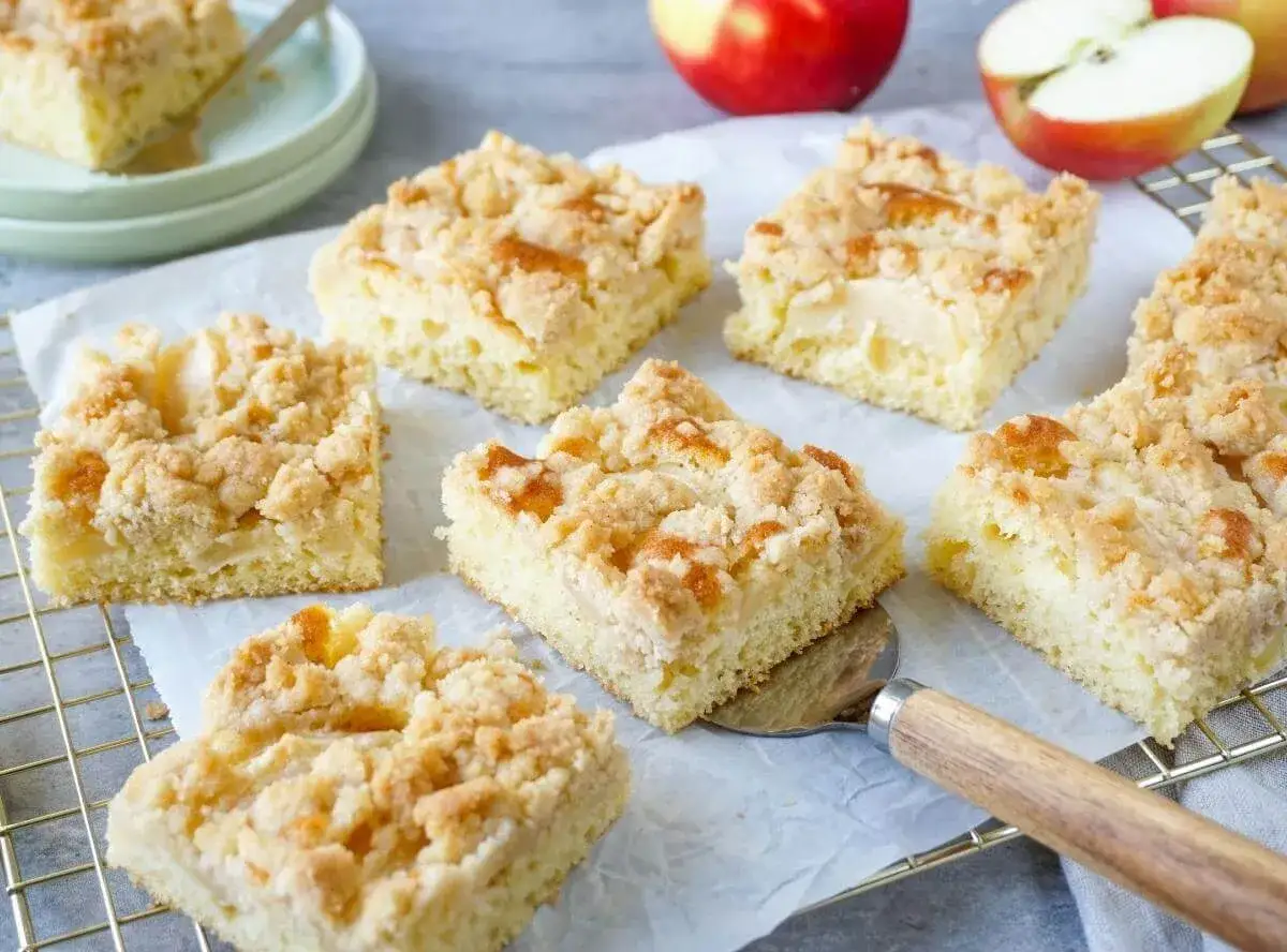 Saftiger Apfelkuchen vom Blech mit Streuseln. Ein Stück wird gerade mit einem Kuchenheber herausgehoben.