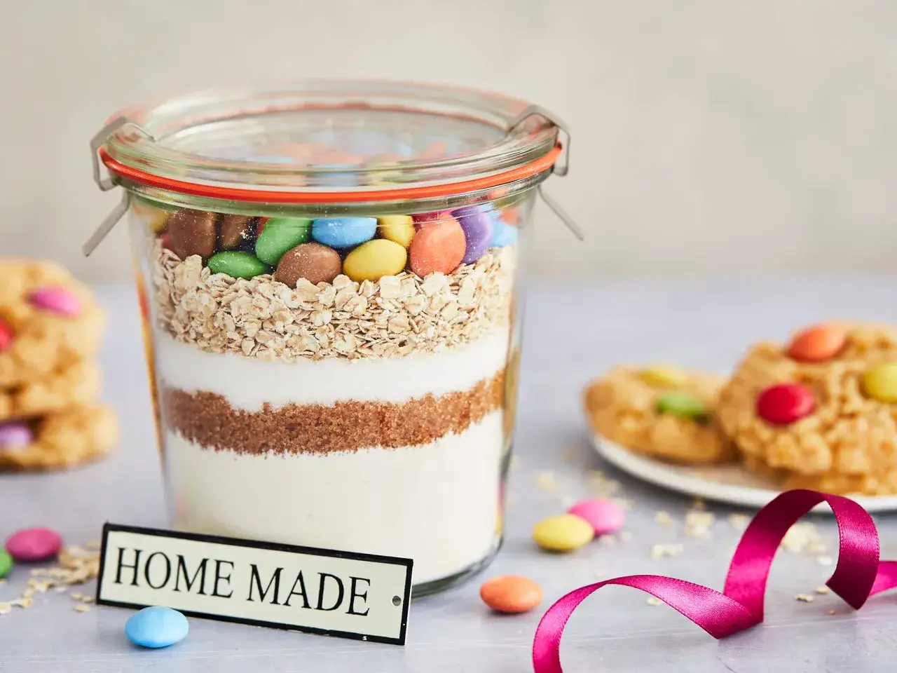 Schichtweise Zutaten für Backmischung im Glas selber machen: Haferflocken, Zucker, Mehl und bunte Schokolinsen. Perfekt als Geschenk!