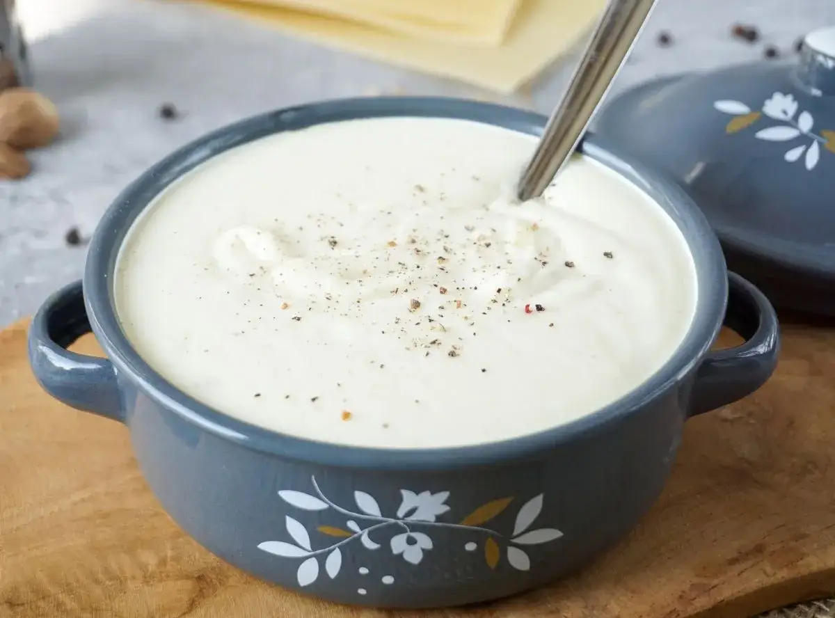 Cremige Béchamelsauce in einer grauen Schüssel, bestreut mit Pfeffer. Perfekt für Lasagne oder Aufläufe.