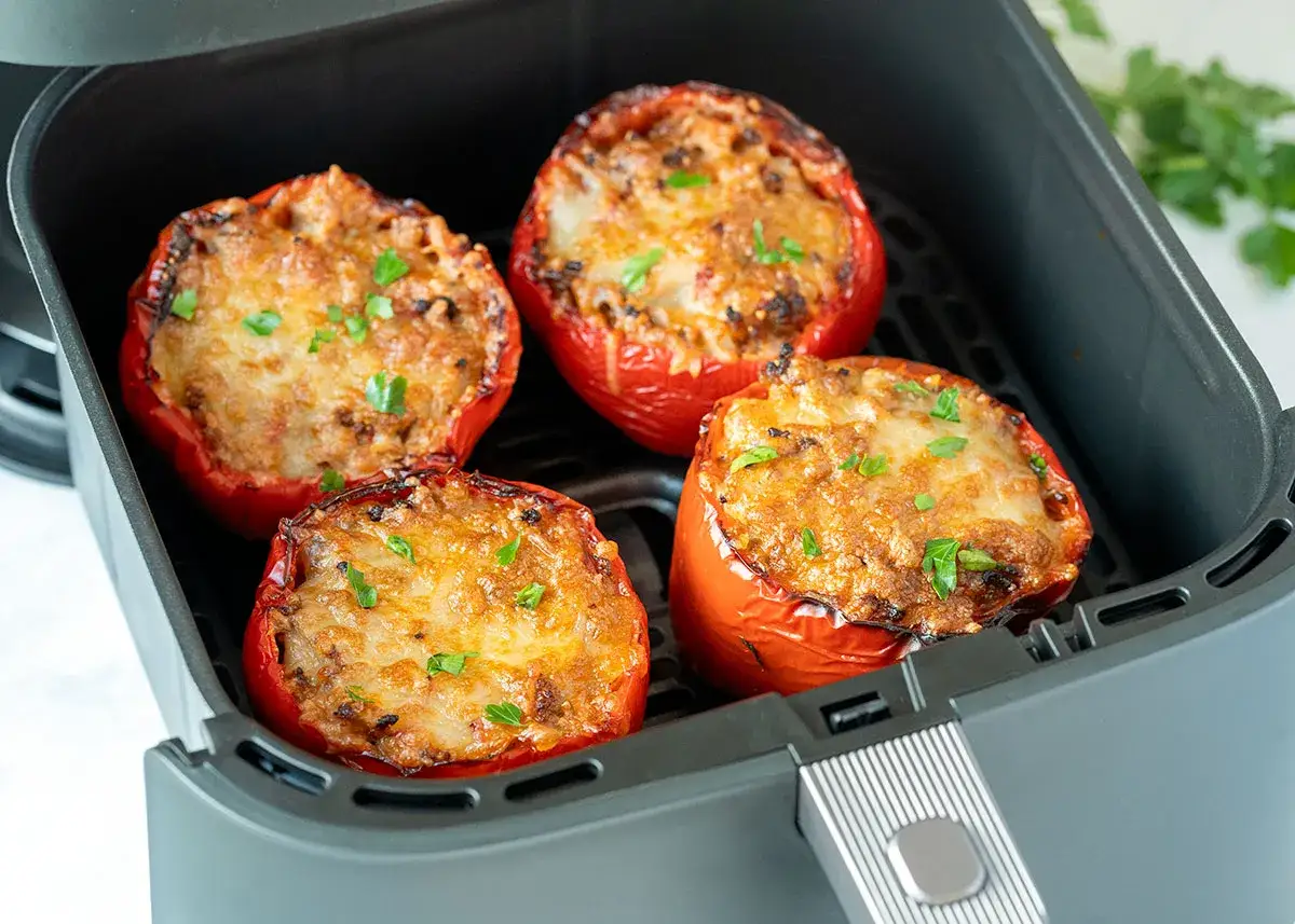 Vier gefüllte Paprikaschoten mit Käse überbacken im Airfryer, garniert mit Petersilie.