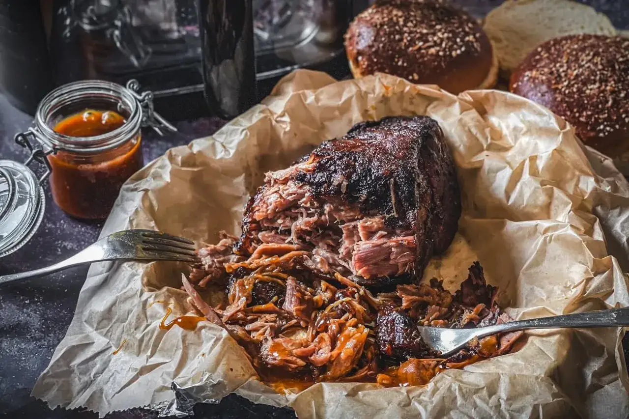 Saftiges pulled pork aus dem Airfryer, zart zerfällt es auf dem Papier. Dazu eine Schale BBQ-Sauce und Burgerbrötchen.