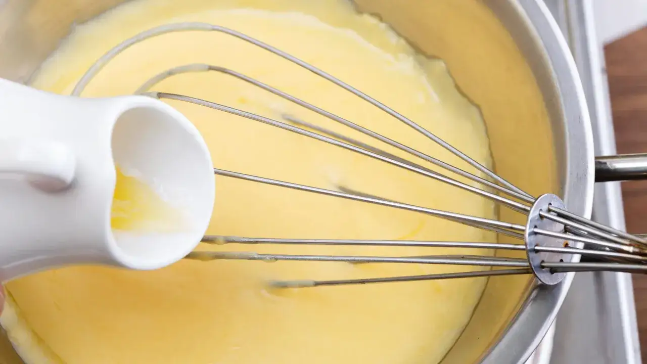 Fl&uuml;ssige Butter wird in eine Sch&uuml;ssel mit einer cremigen, gelben Masse gegossen, w&auml;hrend ein Schneebesen die Zutaten f&uuml;r eine perfekte Sauce Hollandaise vermischt.
