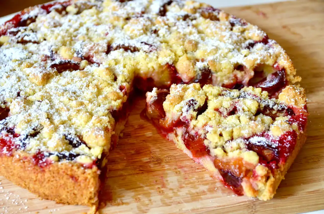 Omas Pflaumenkuchen aus Hefeteig in Springform, mit Streuseln und Puderzucker best&auml;ubt. Ein St&uuml;ck ist herausgeschnitten.