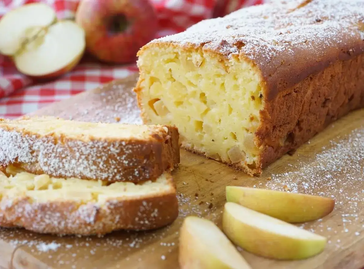 Saftiger Apfelkuchen ohne Zucker mit Quark, bestäubt mit Puderzucker. Daneben liegen frische Apfelspalten.