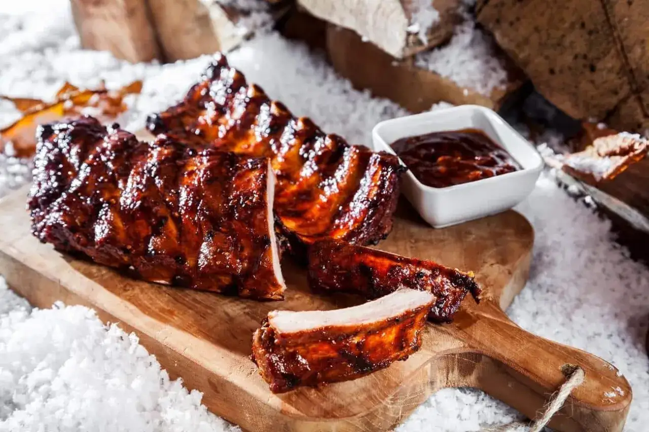 Saftige rippchen im backofen, glasiert und mit BBQ-Sauce, auf einem Holzbrett, umgeben von Schnee und Holz.