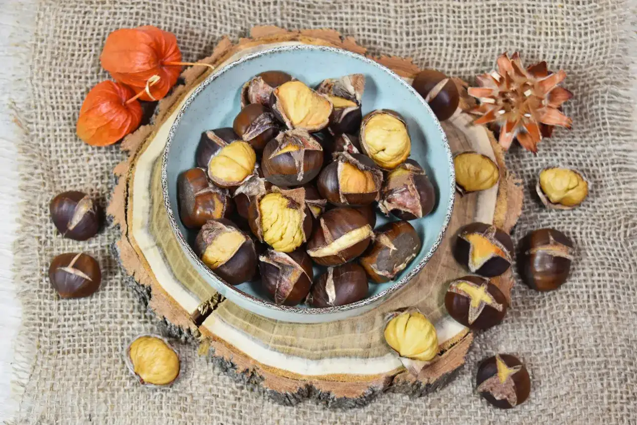 Maronen im Airfryer, frisch und duftend, in einer Schale angerichtet. Ein paar Physalis und eine Zapfen-Deko runden das herbstliche Bild ab.