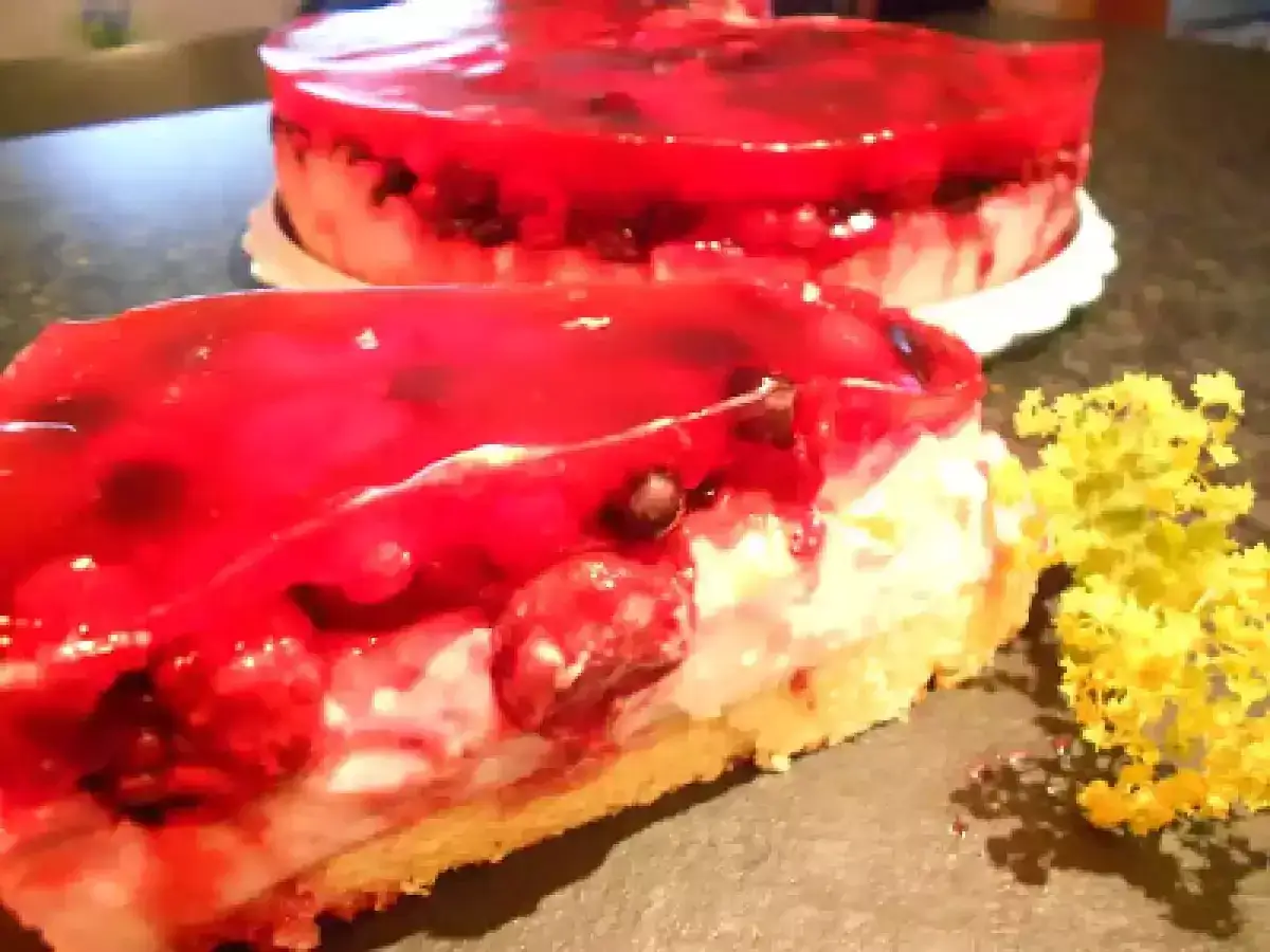Ein St&uuml;ck Kuchen mit Mascarpone, Beeren und rotem Tortenguss. Ein ganzer Kuchen steht im Hintergrund.