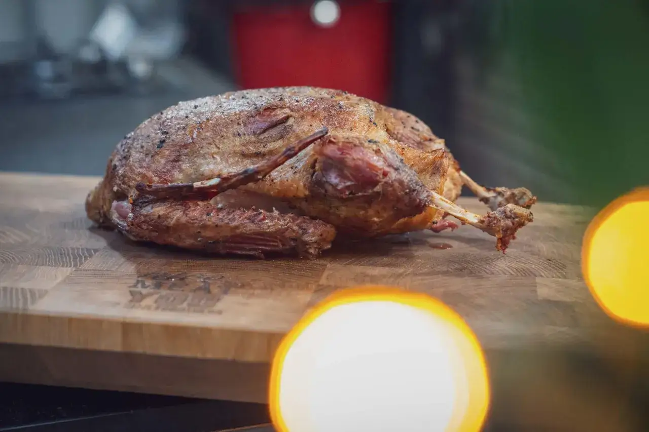 Eine perfekt gegarte Ente, zubereitet sous vide, liegt auf einem Holzbrett. Ihre Haut ist goldbraun und knusprig, mit feinen Gewürzen bestreut.