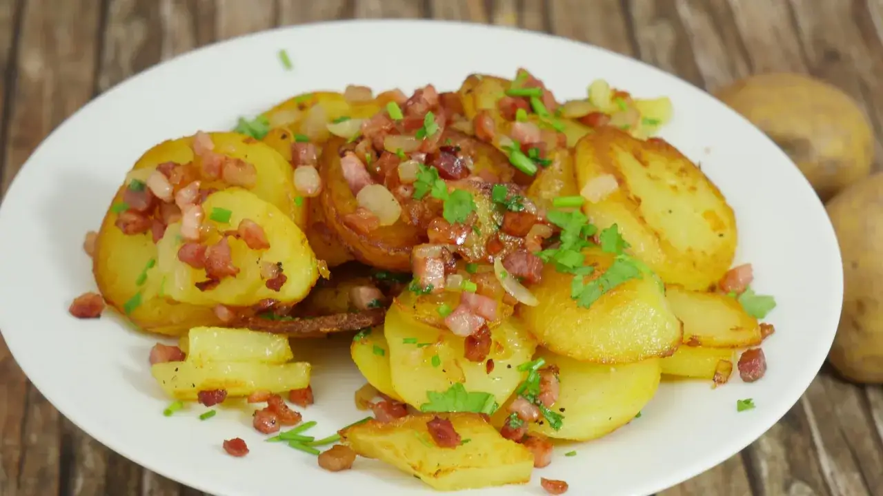 Goldbraune bratkartoffeln im Airfryer, garniert mit Speckwürfeln und frischen Kräutern, auf einem weißen Teller.