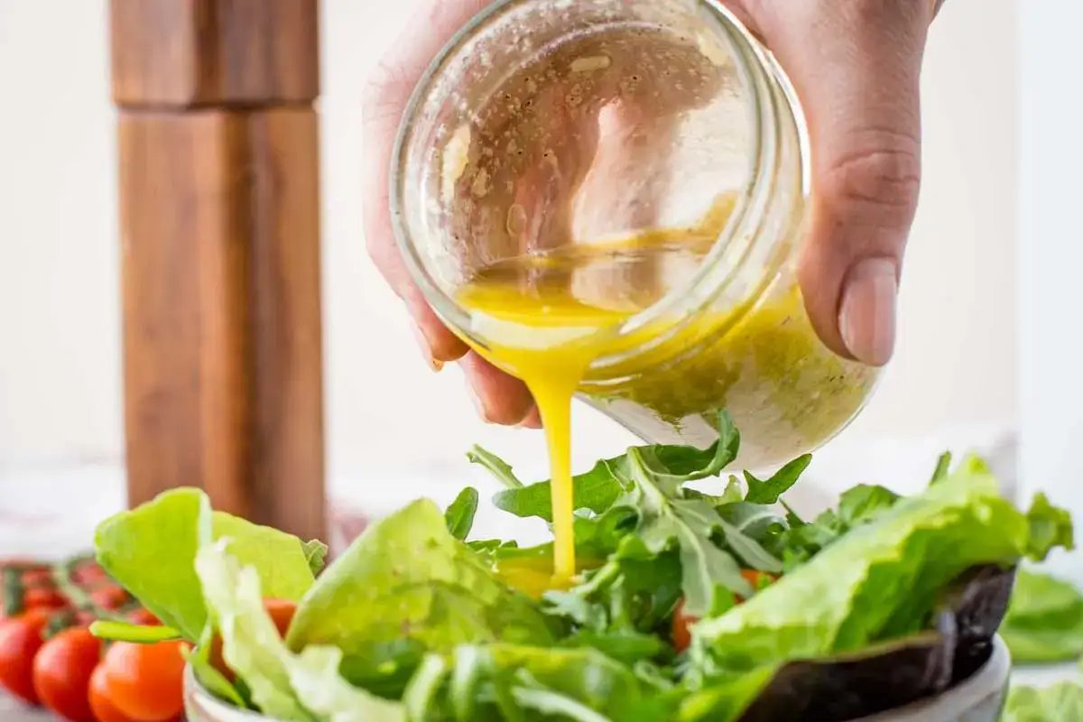 Ein einfaches Vinaigrette Rezept: Gelbe, hausgemachte Vinaigrette wird aus einem Glas &uuml;ber einen frischen Salat gegossen.