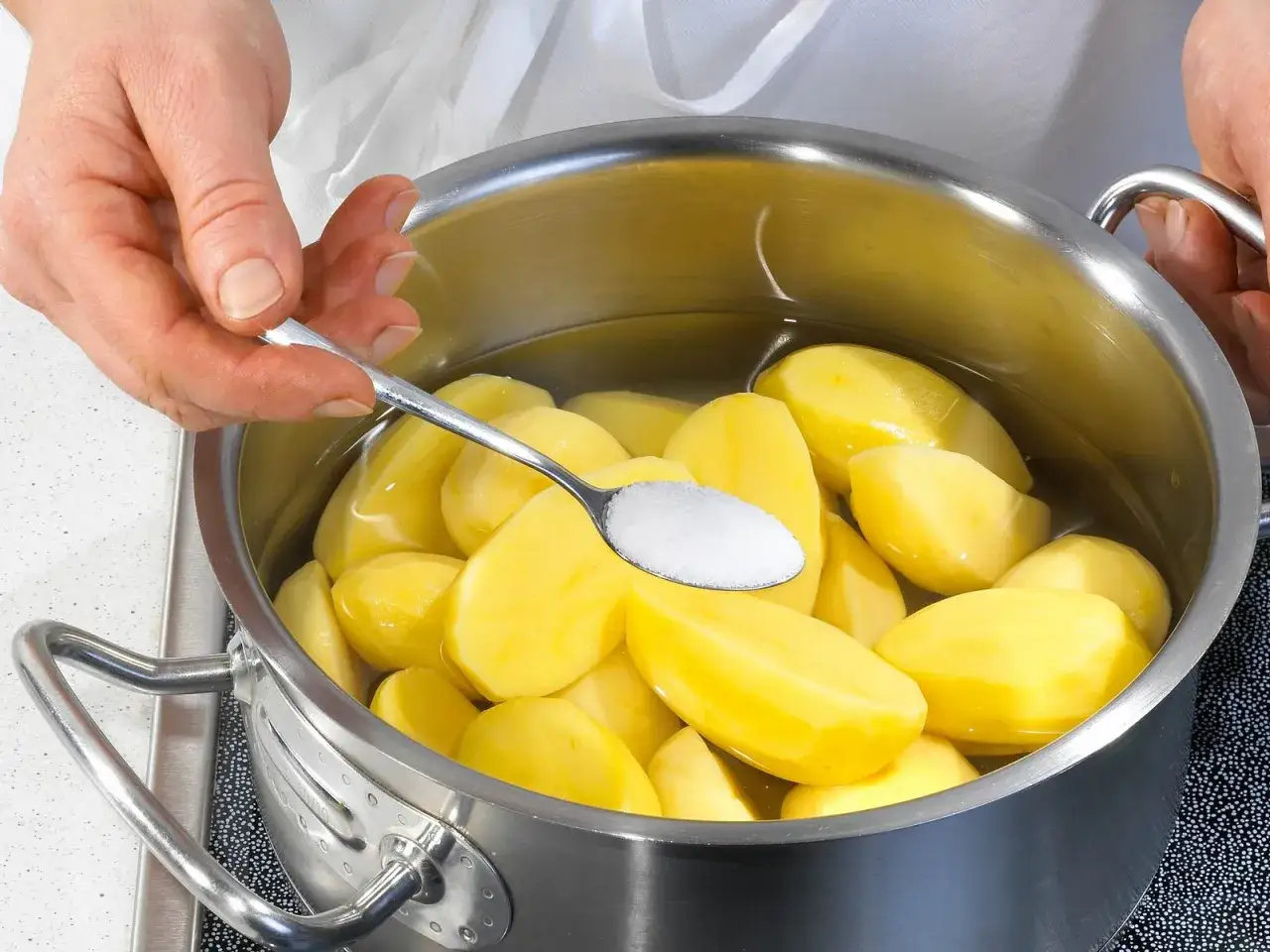 Hände geben Salz zu festkochenden Kartoffeln in einem Topf mit Wasser.