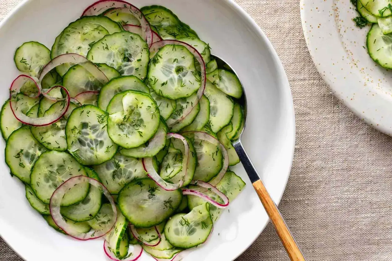 Frischer gurkensalat mit dill und roten Zwiebelringen, serviert in einer wei&szlig;en Sch&uuml;ssel.