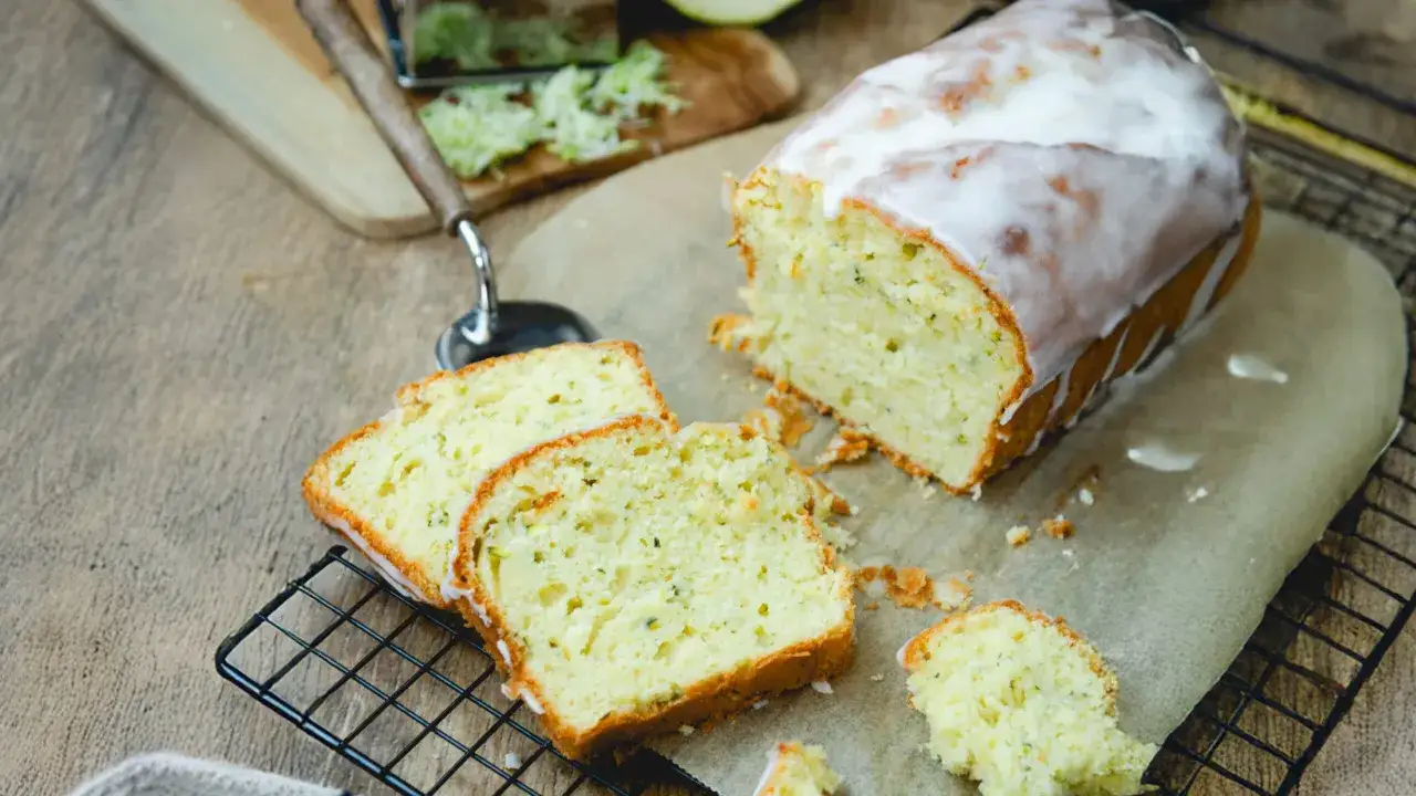 Saftiger Zucchini Kuchen mit Zuckerguss, frisch gebacken und angeschnitten. Ein Stück vom Kuchen liegt daneben.