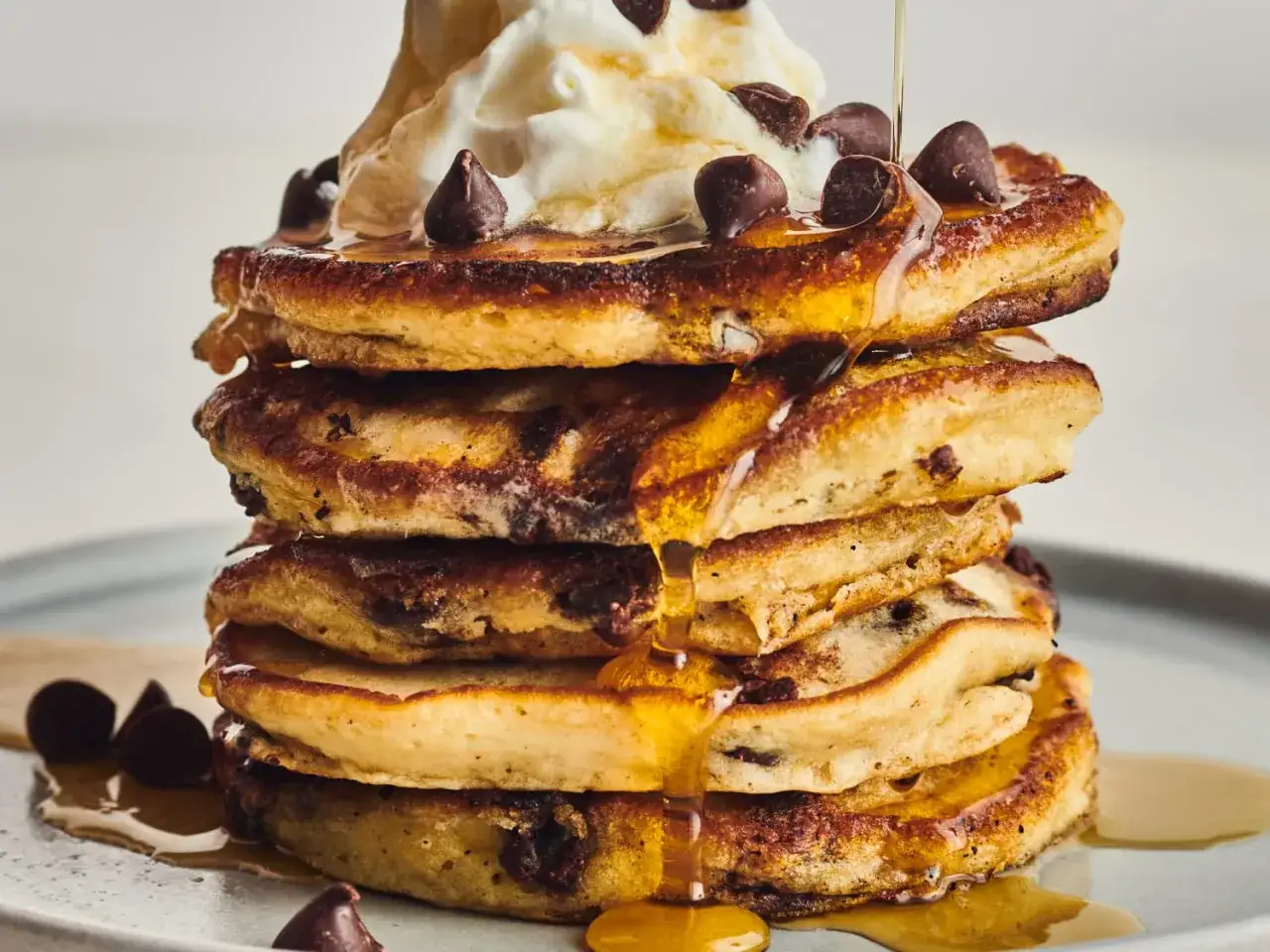 Ein Stapel saftiger Schokoladenst&uuml;ckchen-Pfannkuchen, &uuml;bergossen mit Sirup und Sahne. Ein Genuss f&uuml;r jeden Morgen!
