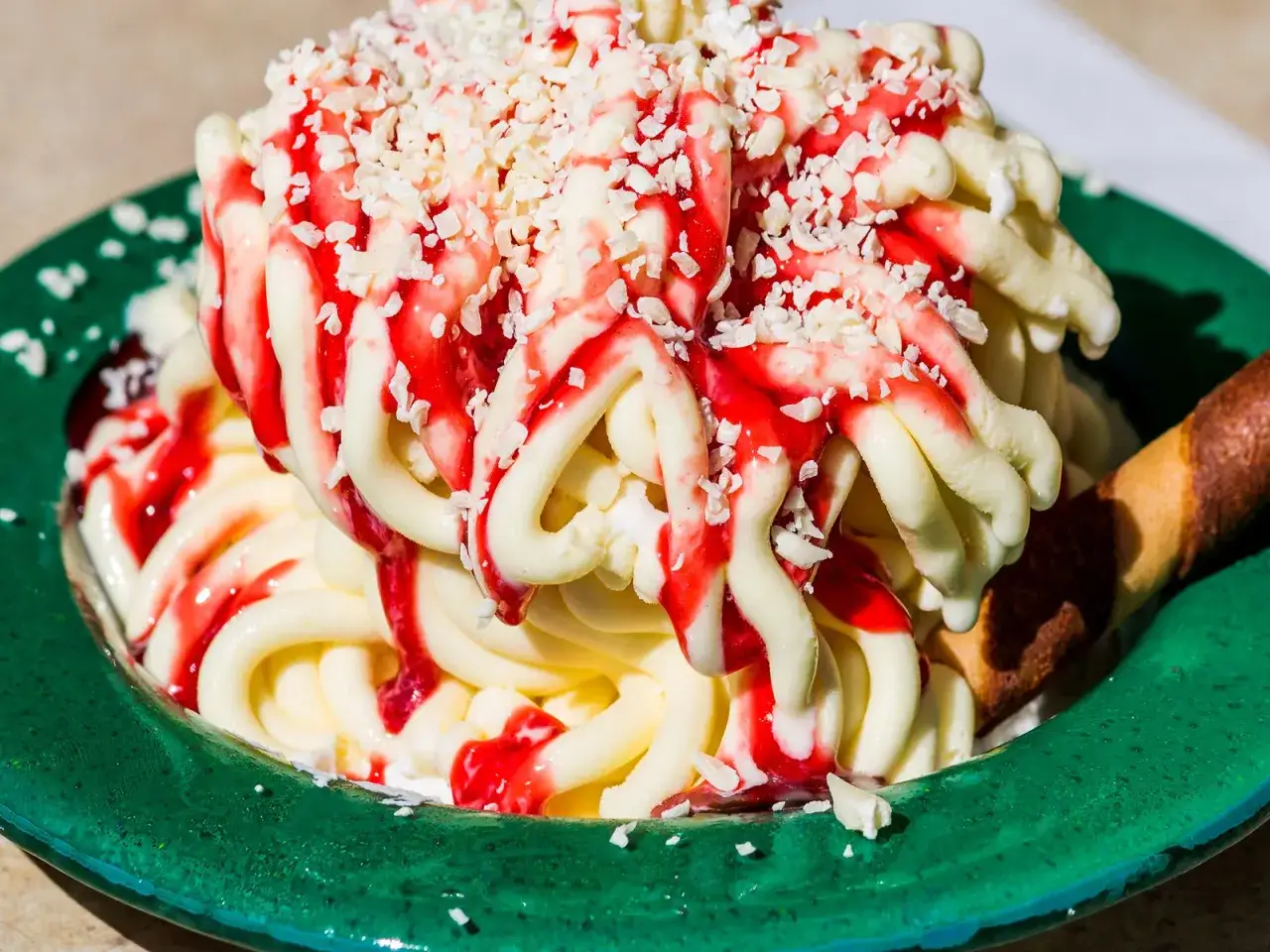 Ein k&ouml;stliches Spaghetti-Eis-Dessert mit Erdbeersauce und wei&szlig;en Schokost&uuml;ckchen in einer gr&uuml;nen Schale.